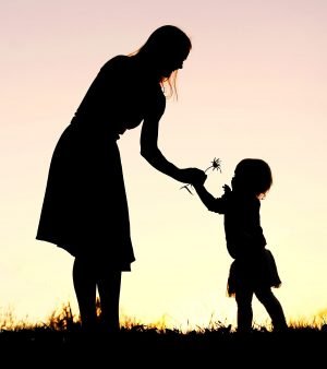 Woman giving flower to child at sunset